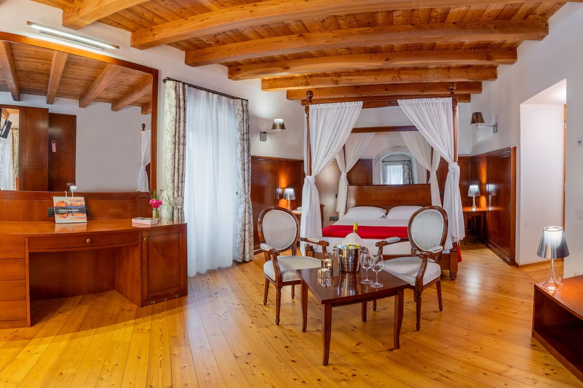 A wooden-floored bedroom with a four-poster bed, a desk with a mirror, and two bedside tables with lamps.