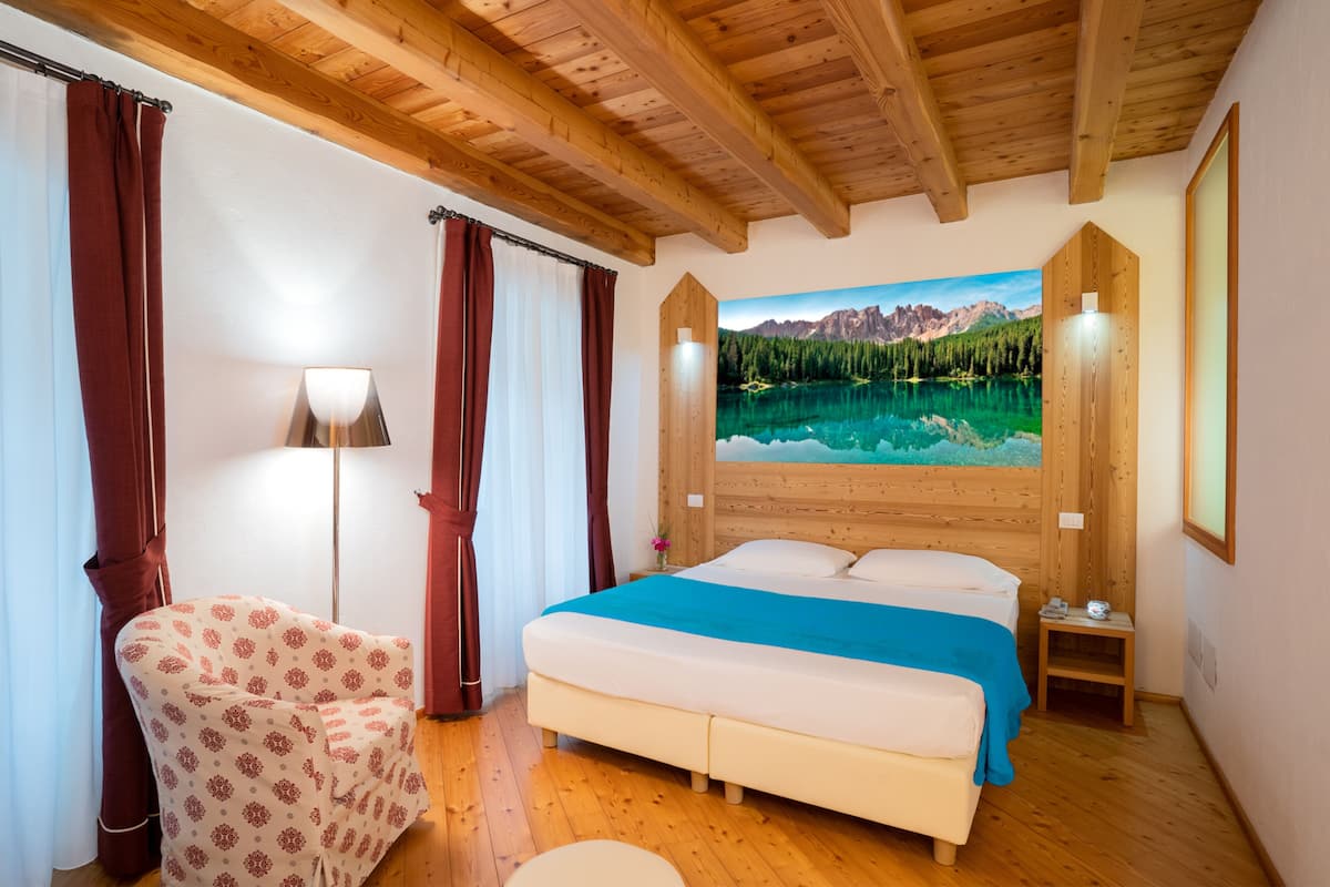 A bedroom with a bed, a chair, a lamp, and a painting of a mountain landscape.