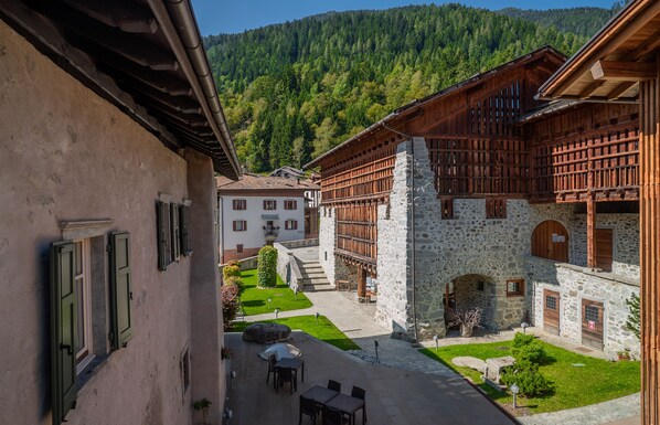 Une cour bordée de bâtiments en pierre, un petit jardin et une vue sur une montagne boisée.