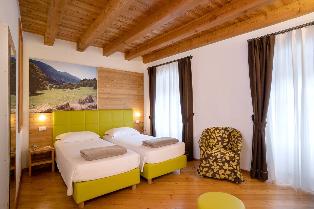 A room with two beds, a chair, wooden floors, a wooden ceiling, and a painting of a landscape.