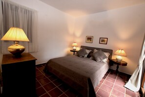 Ein ordentlich bezogenes Bett mit einem gemusterten Überwurf, zwei Nachttischlampen und ein kleiner Tisch mit einer Lampe.