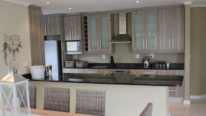 A modern kitchen with a central island, wicker chairs, and a dining table. - Golf Paradise, Langebaan 6-sleeper (Langebaan)