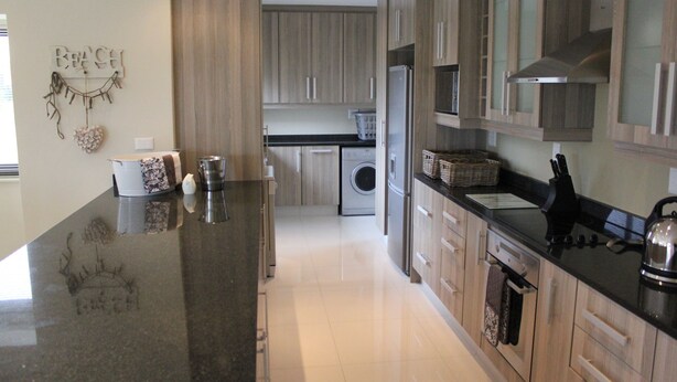 A modern kitchen with granite countertops, wooden cabinets, a built-in washing machine, and a stainless steel range hood. - Golf Paradise, Langebaan 6-sleeper (Langebaan)
