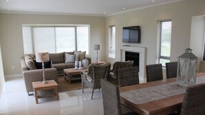 A modern living room with a sofa, coffee table, wicker chairs, a dining table, and a fireplace. - Golf Paradise, Langebaan 6-sleeper (Langebaan)