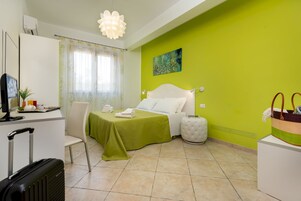 A hotel room with a bed, a desk, a chair, a suitcase, and a painting on the wall.
