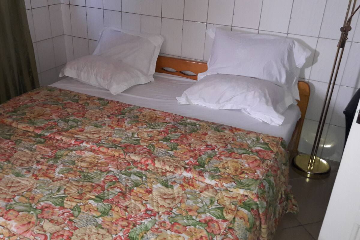 Ein Bett mit floralem Überwurf, weißen Kissen und einem hölzernen Kopfteil.