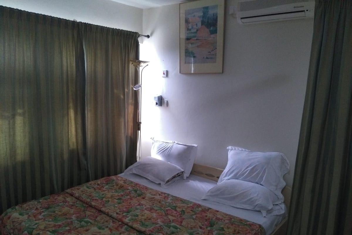 Ein Hotelzimmer mit Bett, floralem Überwurf, weißen Kissen, einem Gemälde an der Wand und einer Klimaanlage.