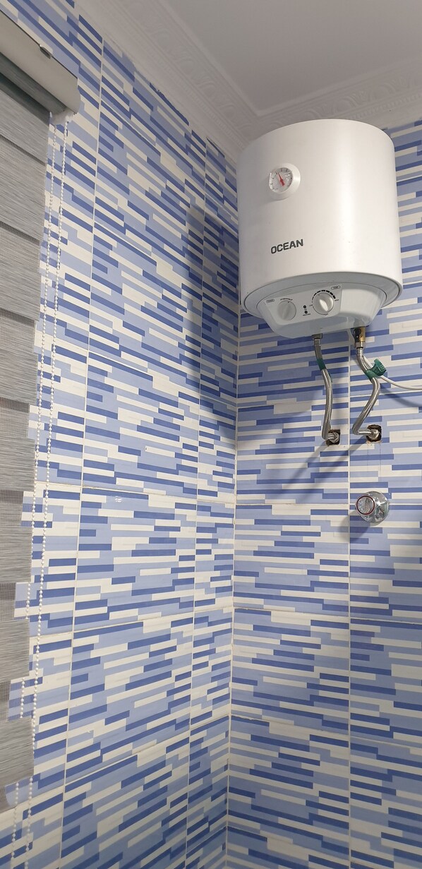 A bathroom with a white water heater labeled 'OCEAN' mounted on a wall with blue and white patterned tiles.