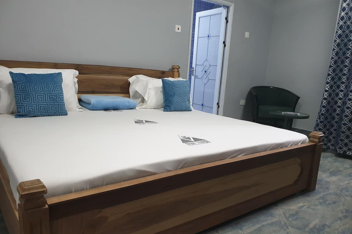 Ein ordentlich bezogenes Bett mit Holzbettgestell, einer weißen Matratze und gemusterten Kissen.