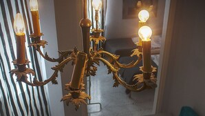 A room with a teal sofa, a chandelier with multiple light bulbs, and a herringbone-patterned floor. - Koro de Varsovio - Chmielna 6 (Warsaw)