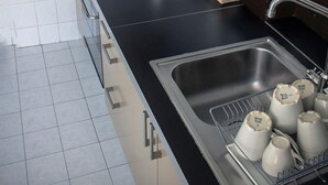 A modern kitchen with a black countertop, stainless steel sink, and a dish rack with cups. - Koro de Varsovio - Chmielna 6 (Warsaw)