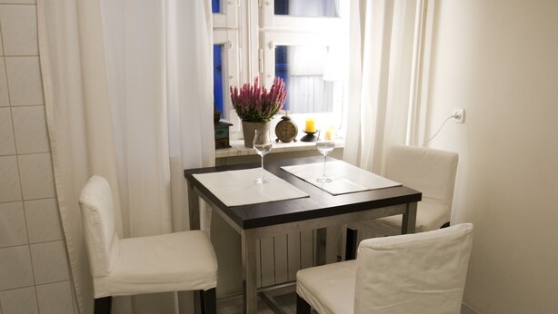 A small dining area with a table and two chairs, a potted plant, a candle, and a clock on the windowsill. - Koro de Varsovio - Chmielna 6 (Warsaw)