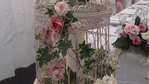 Un présentoir à gâteaux à plusieurs niveaux, décoré de roses et de verdure, placé sur un fond blanc et illuminé de guirlandes lumineuses.
