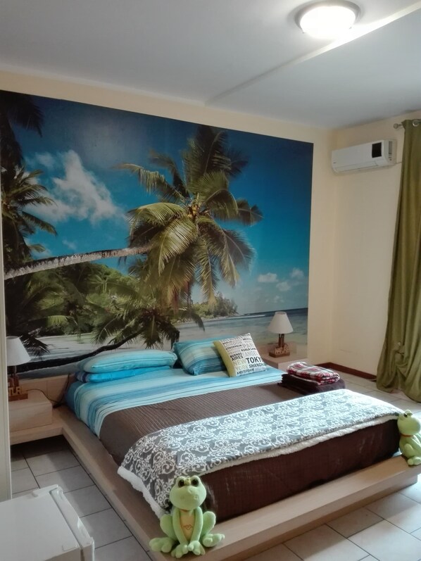 A bedroom with a bed, a wall mural of a beach scene, a green curtain, and a small green frog toy on the bed. - B&B Santa Sofia (Gravina di Catania)
