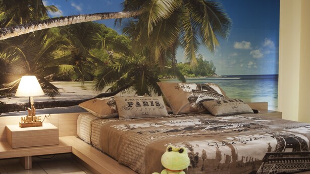 Une chambre à coucher avec une fresque murale sur le thème de la plage, un jouet en forme de grenouille en peluche et une lampe sur une table de chevet.