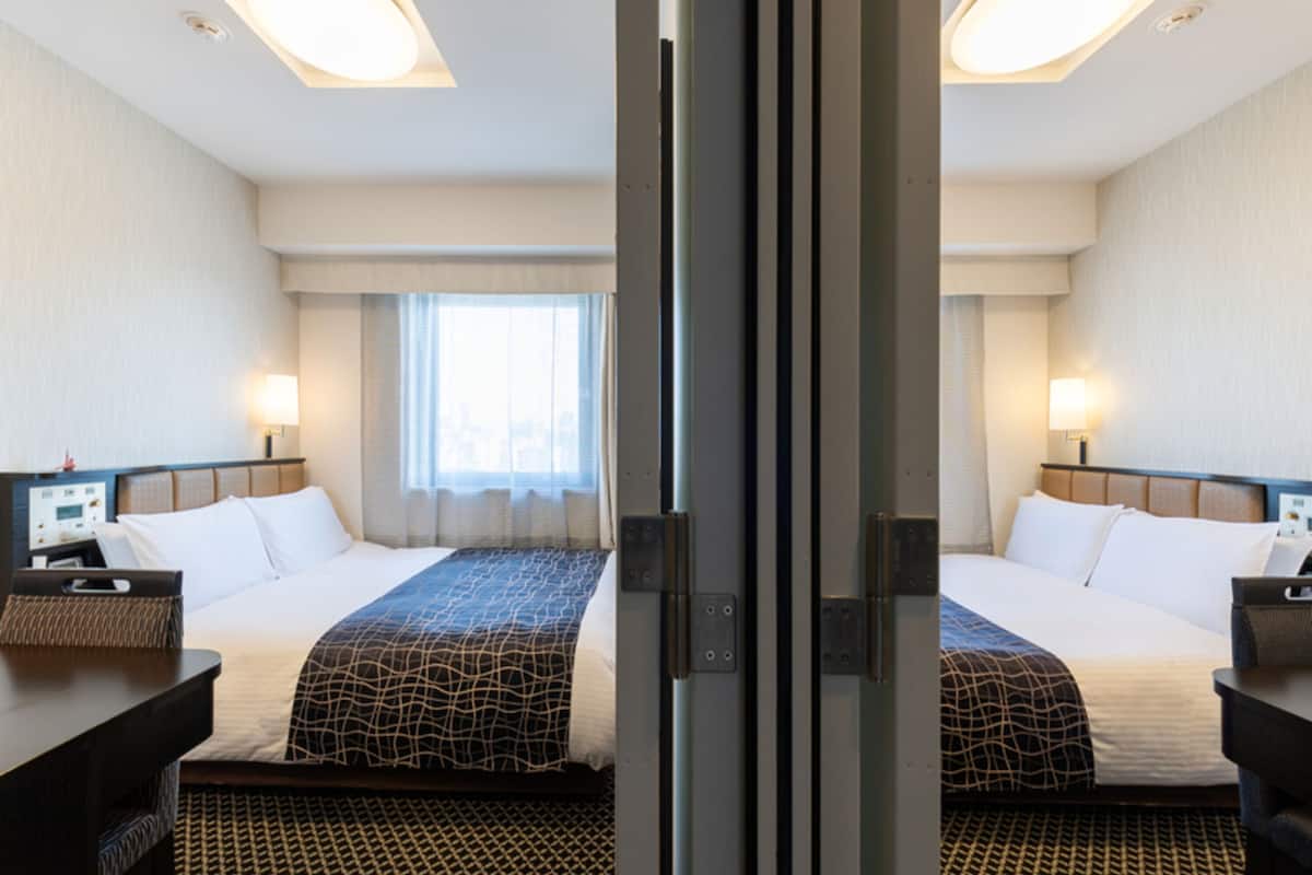 Hotellihuone, jossa on kaksi sänkyä, työpöytä ja ikkuna, jossa on verhot.