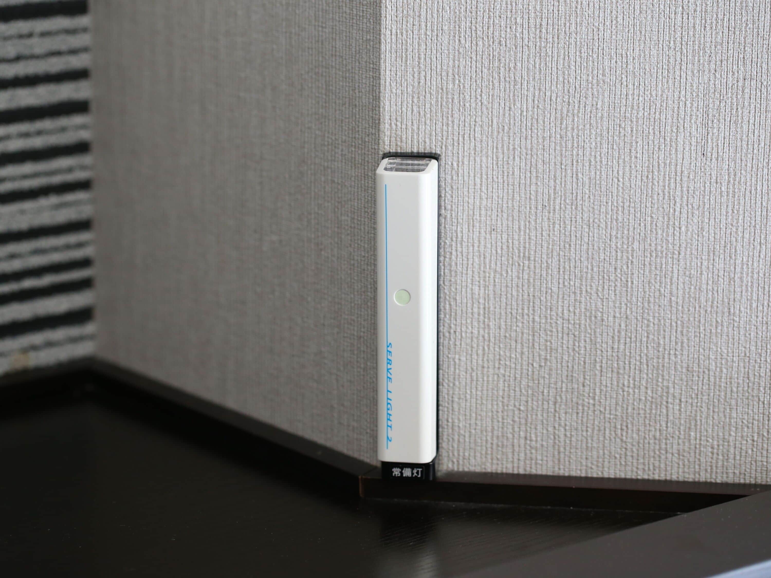 A device with a blue light indicator, possibly a charging or power station, placed on a dark surface against a textured wall.