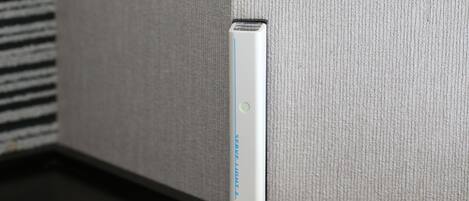 A device with a blue light indicator, possibly a charging or power station, placed on a dark surface against a textured wall.