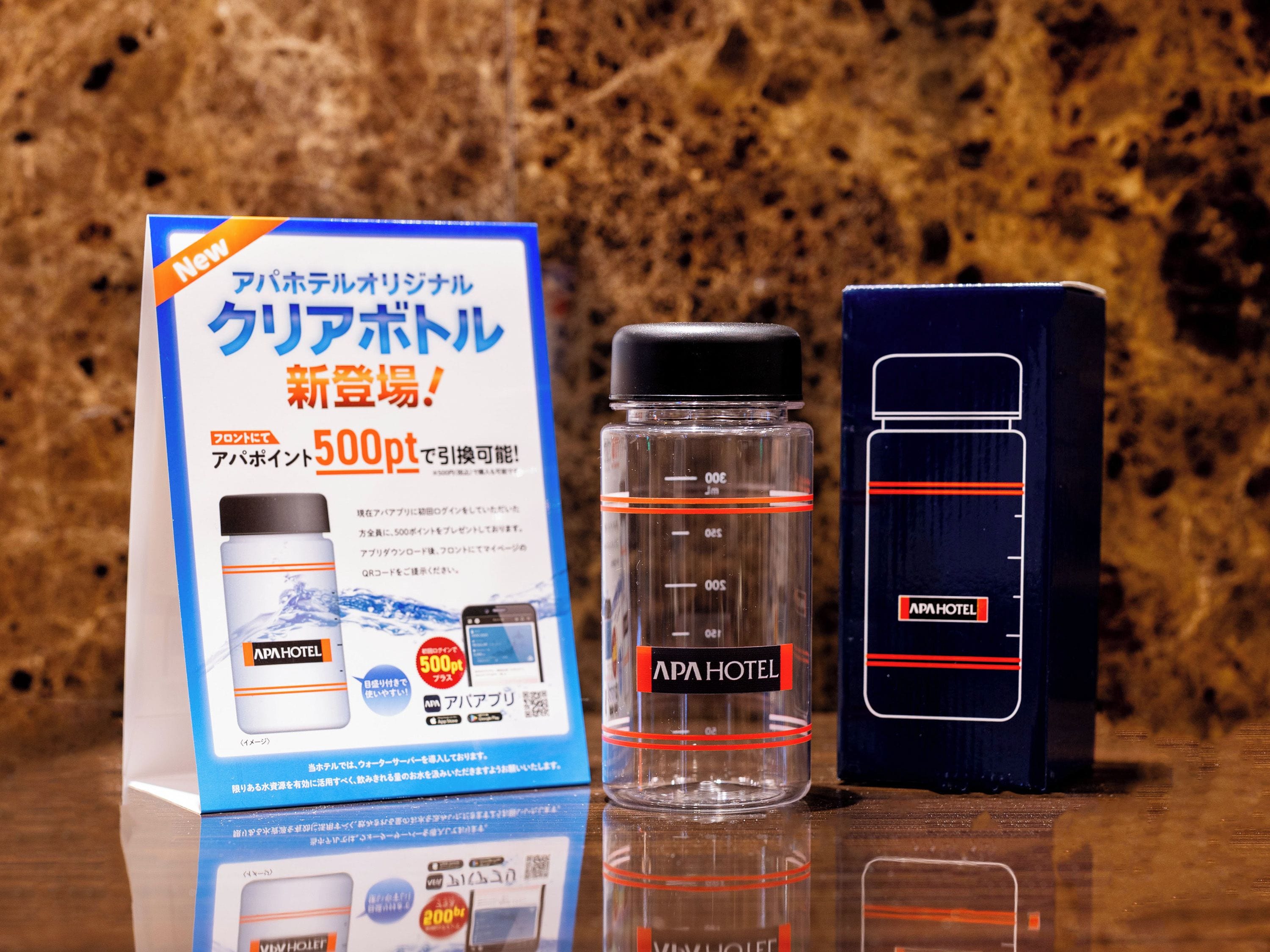 A promotional display for a hotel product, including a bottle and a box, with Japanese text and a QR code.