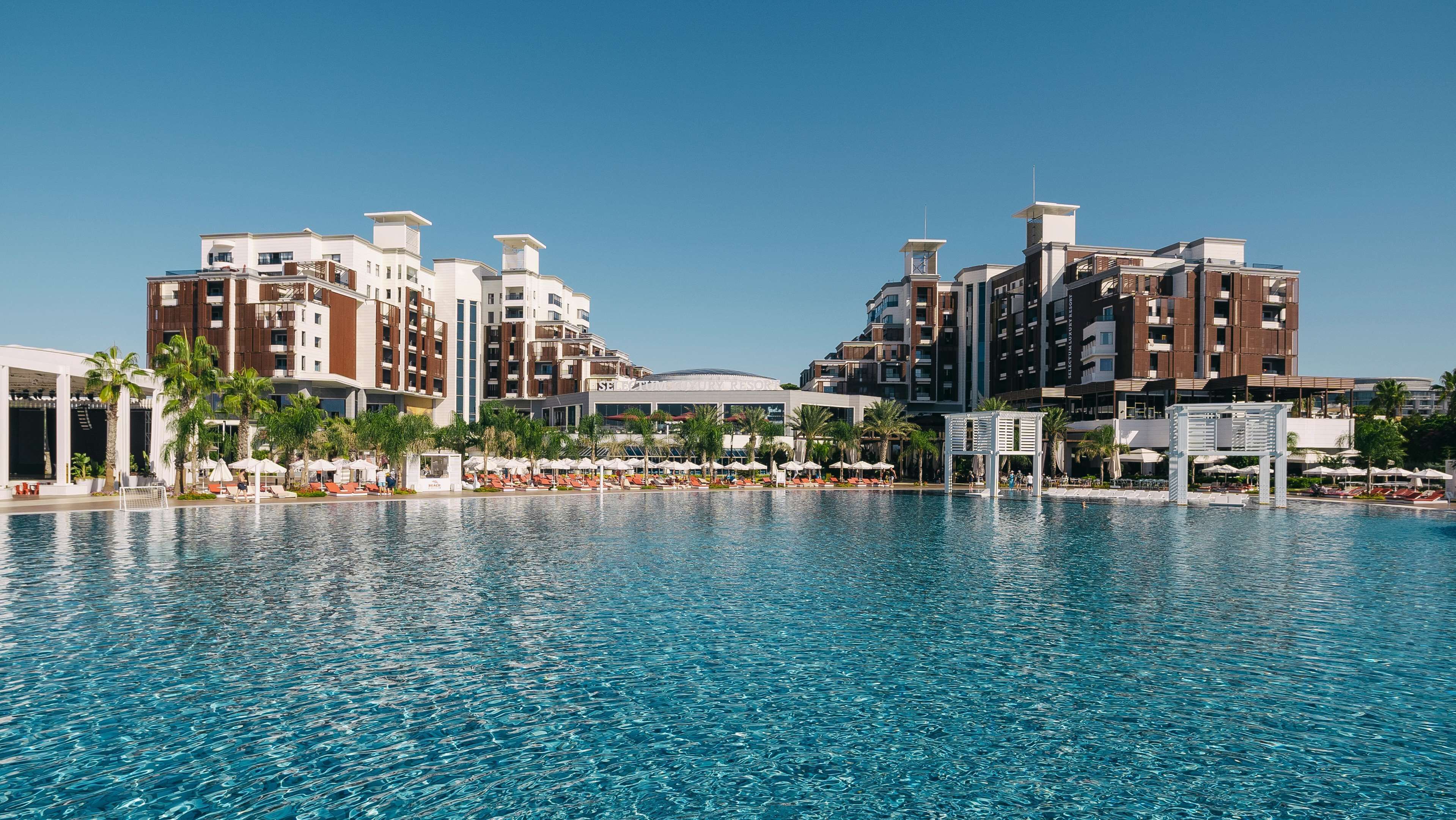 A hotel with a large pool, multiple buildings, and palm trees.