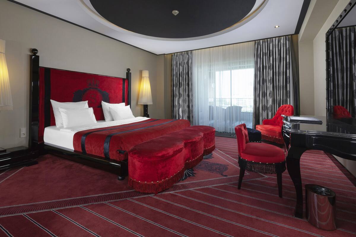 Una habitación de hotel con una cama grande, cabecera tapizada de rojo, un escritorio con una silla y un espejo grande.