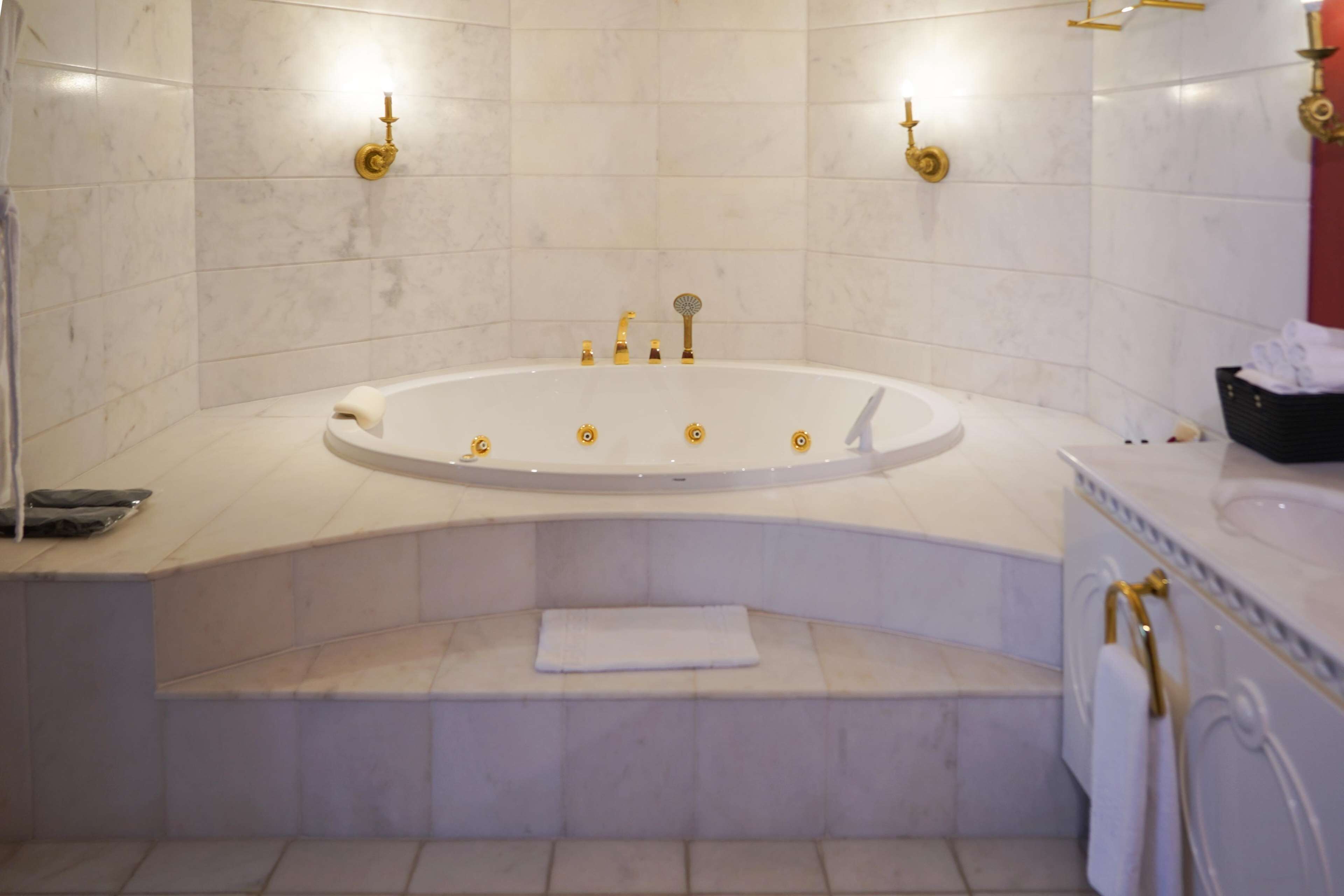 A bathroom with a freestanding bathtub, marble walls, and gold fixtures.