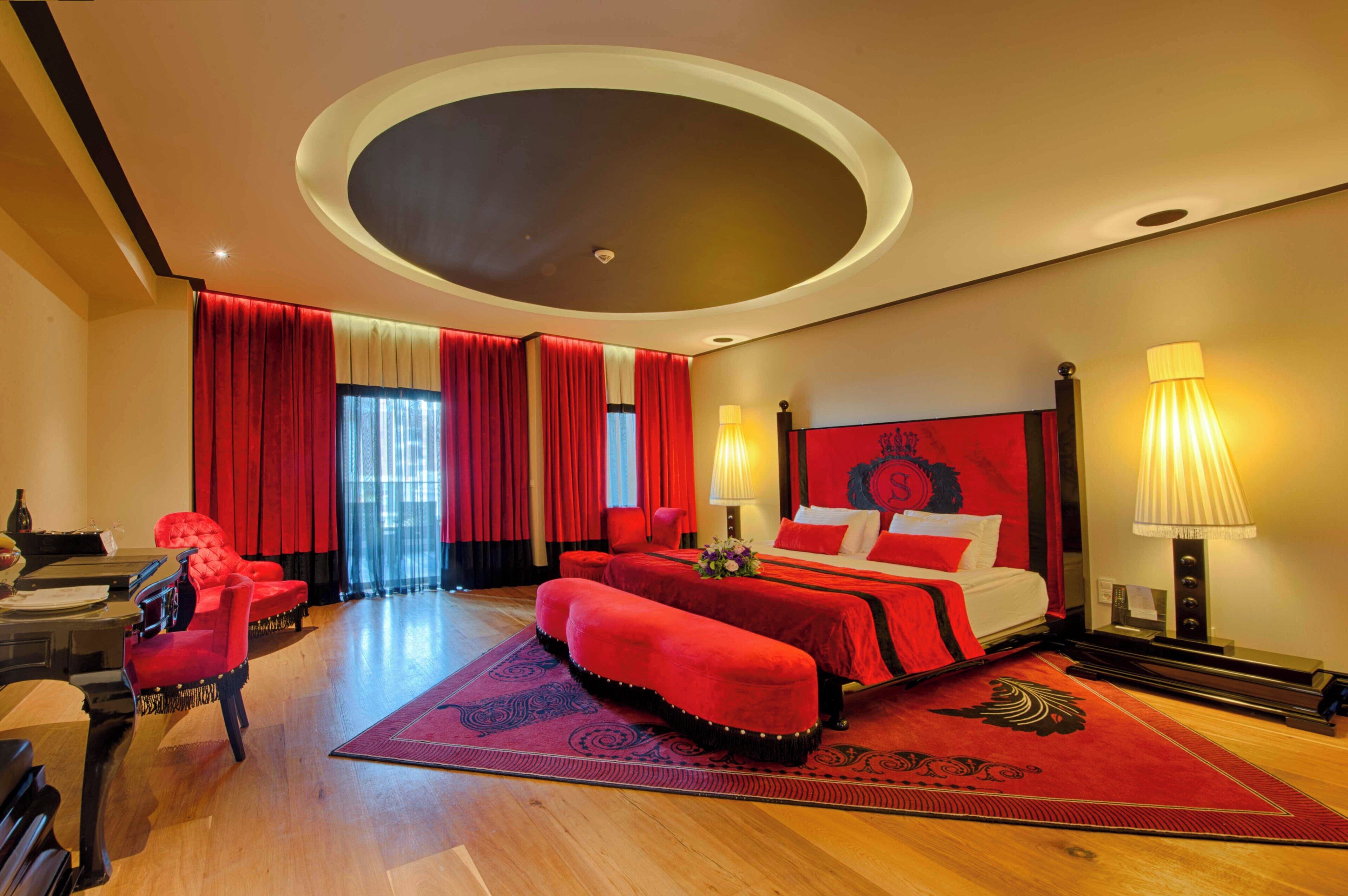 A hotel room with a bed, a red sofa, a piano, and a large window with curtains.