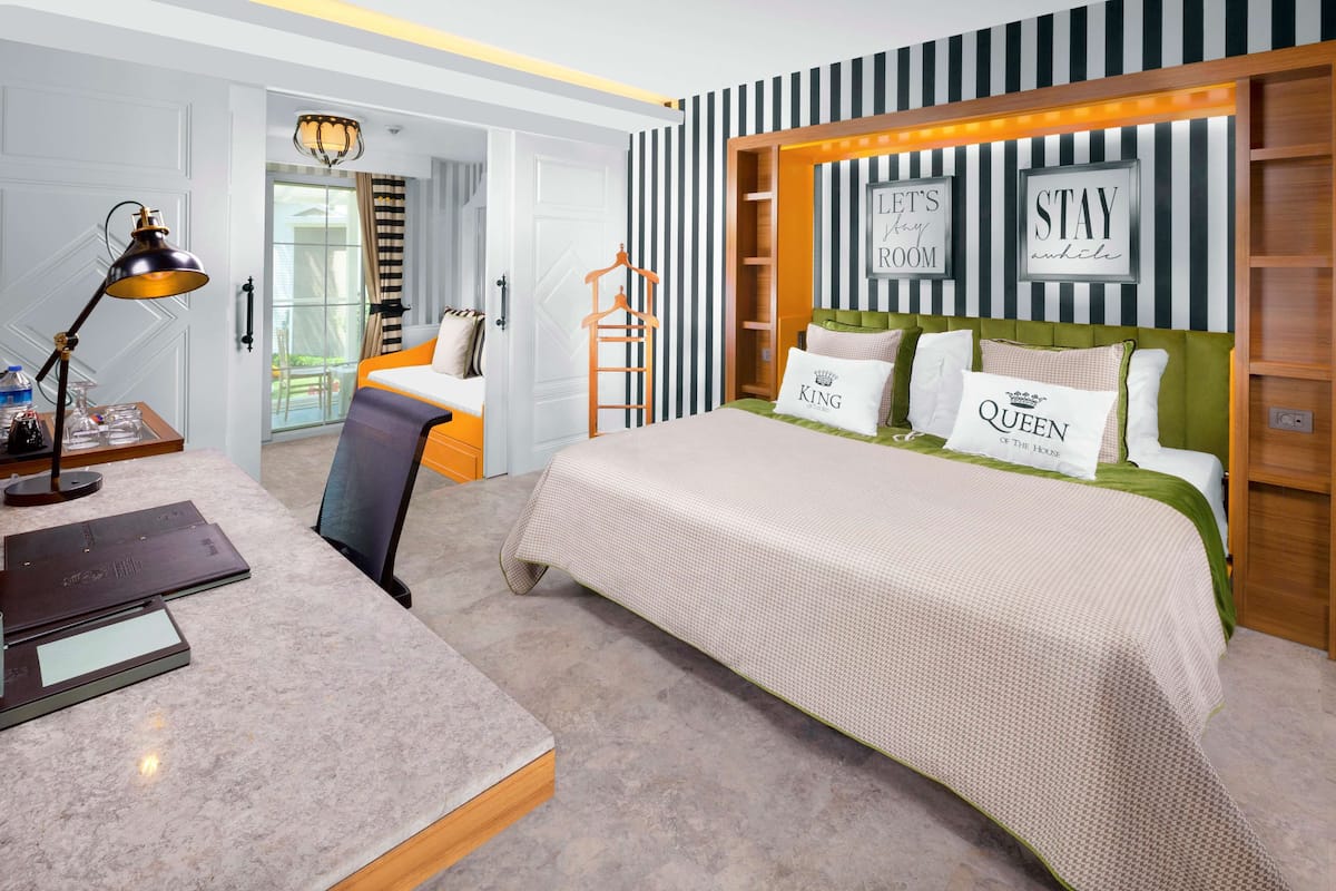 Una habitación de hotel con cama, escritorio con lámpara, silla y armario.