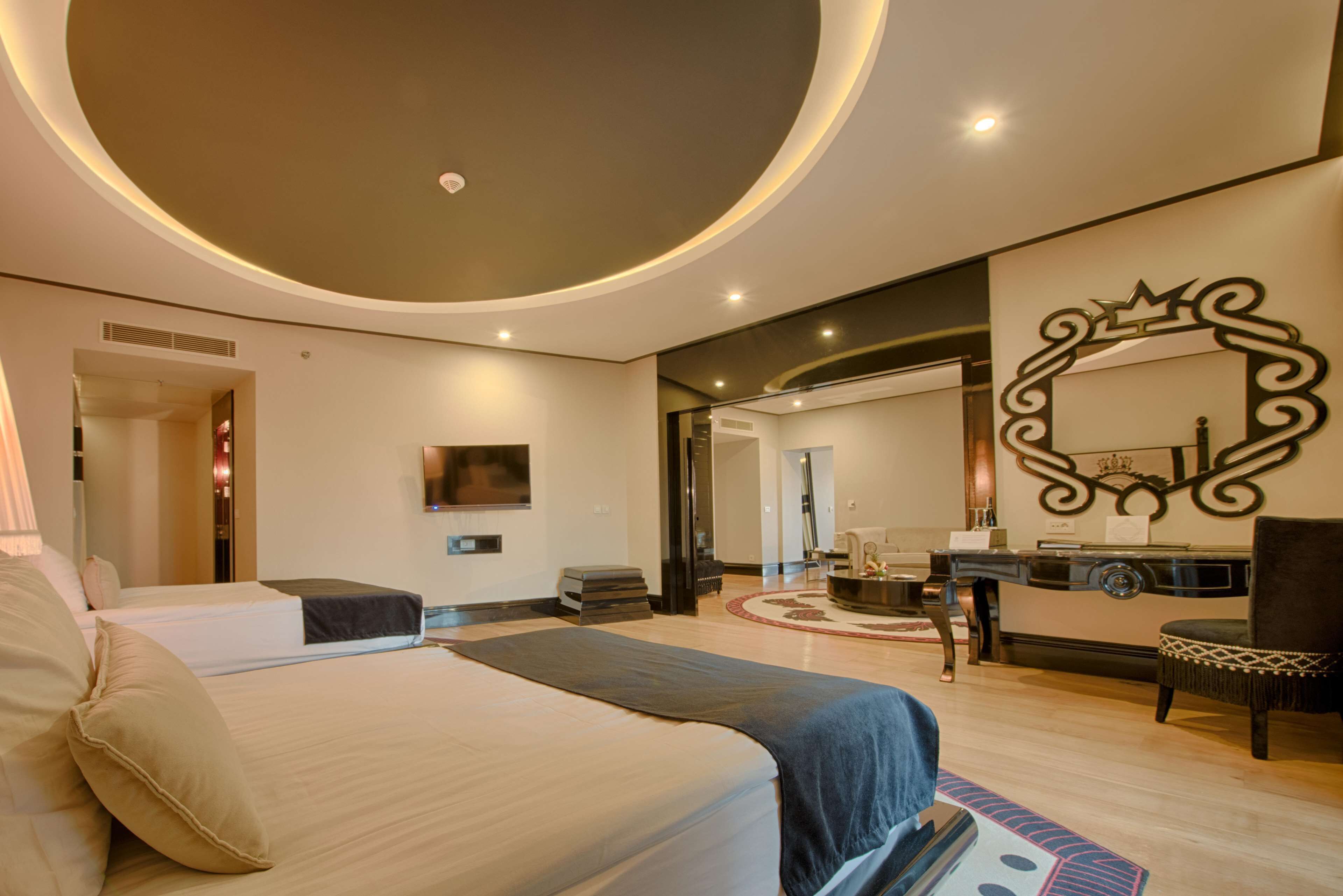 A modern hotel room with a large bed, a desk, a chair, and a mirror.