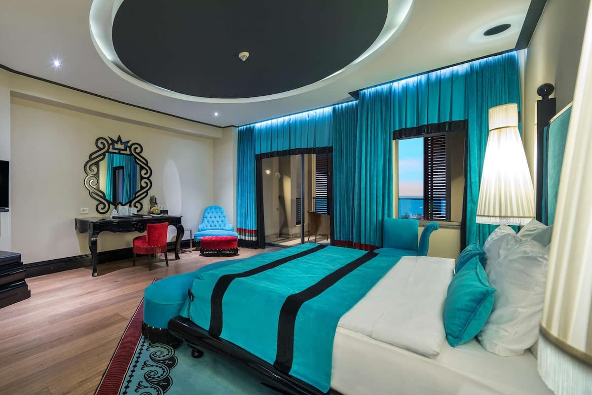 Una habitación de hotel moderna con una cama grande, un televisor de pantalla plana, un escritorio y una zona de estar con una silla roja.