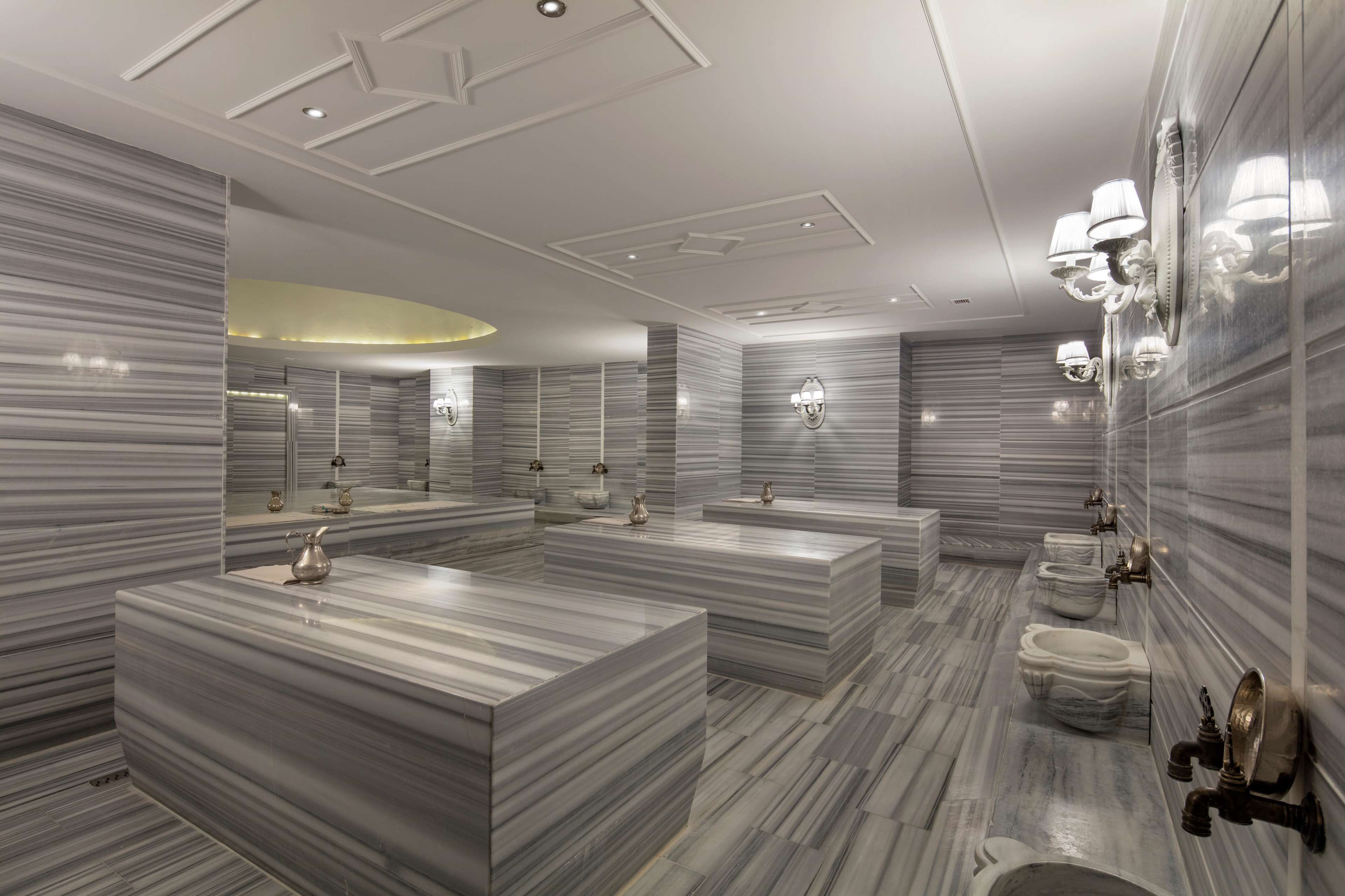 A modern bathroom with marble countertops, multiple sinks, and wall-mounted lighting fixtures.