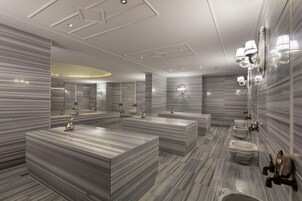 A modern bathroom with marble countertops, multiple sinks, and wall-mounted lighting fixtures.
