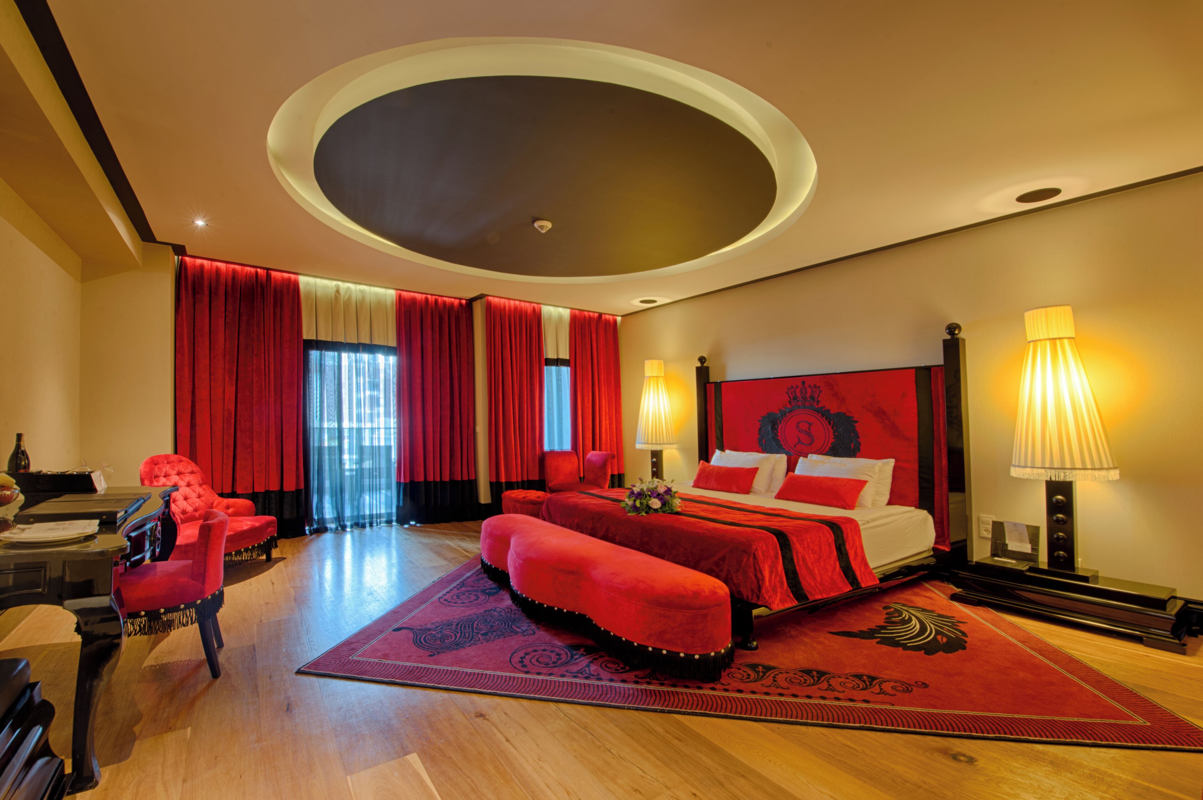 A hotel room with a large bed, a desk with a chair, a piano, and a red carpet.