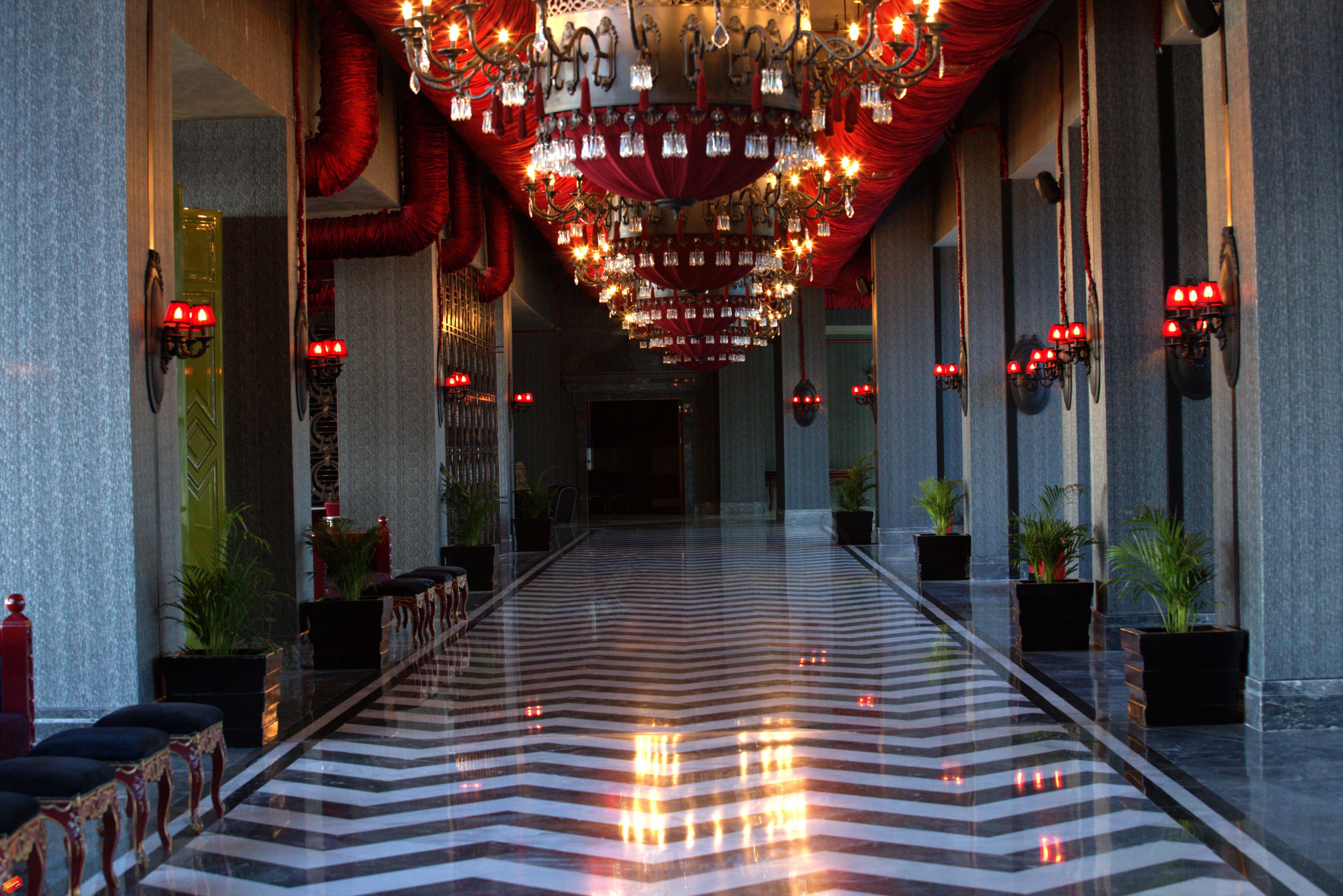 Un pasillo largo y estrecho con piso a rayas negras y blancas, cortinas rojas y varios candelabros.