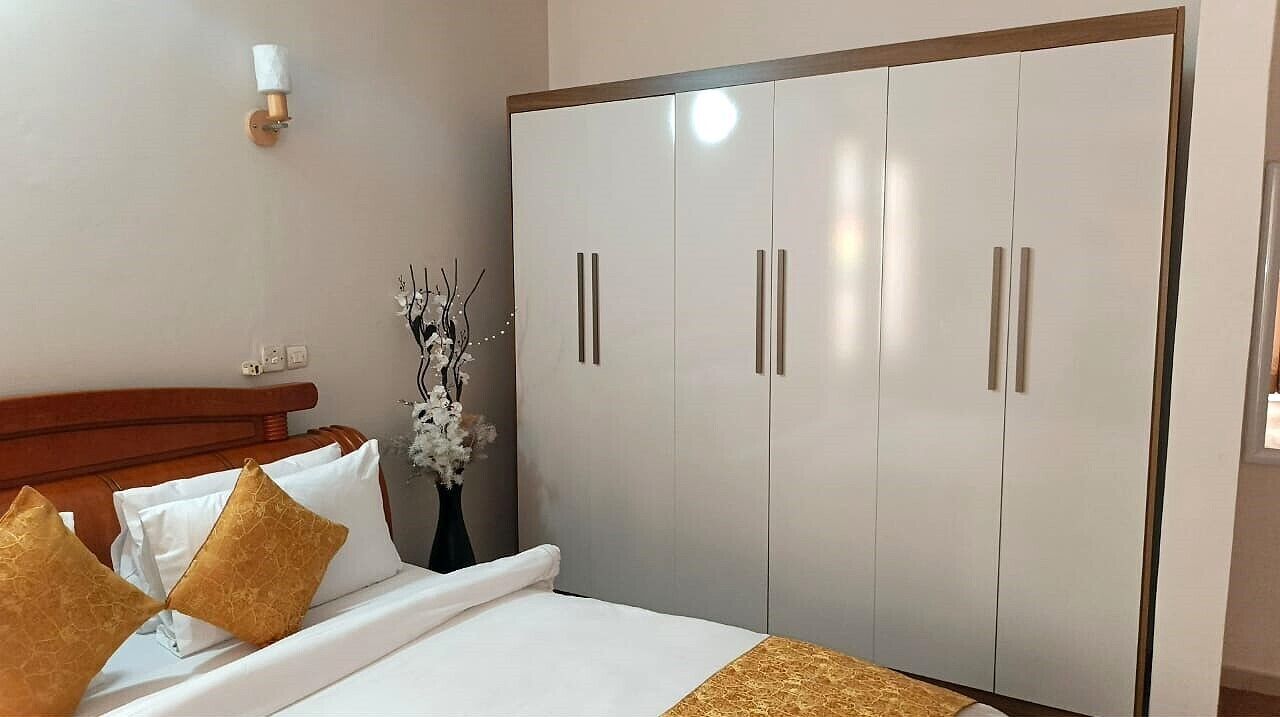 Habitación de hotel con cama, armario, un jarrón con flores y una lámpara de pared.