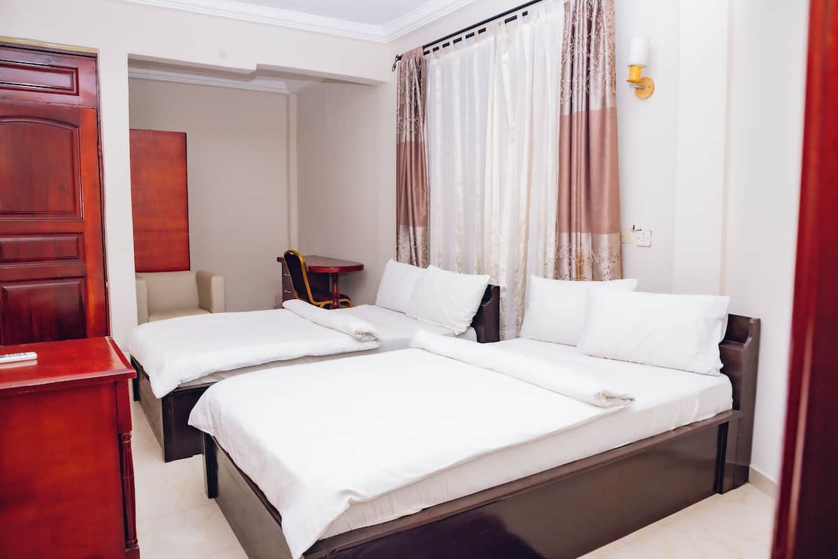 A hotel room with two beds, a wooden desk, a chair, and a painting on the wall.
