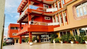 A multi-story hotel with a red and beige facade, multiple balconies, and a parking area with potted plants. - Golden Key Hotel (Accra)