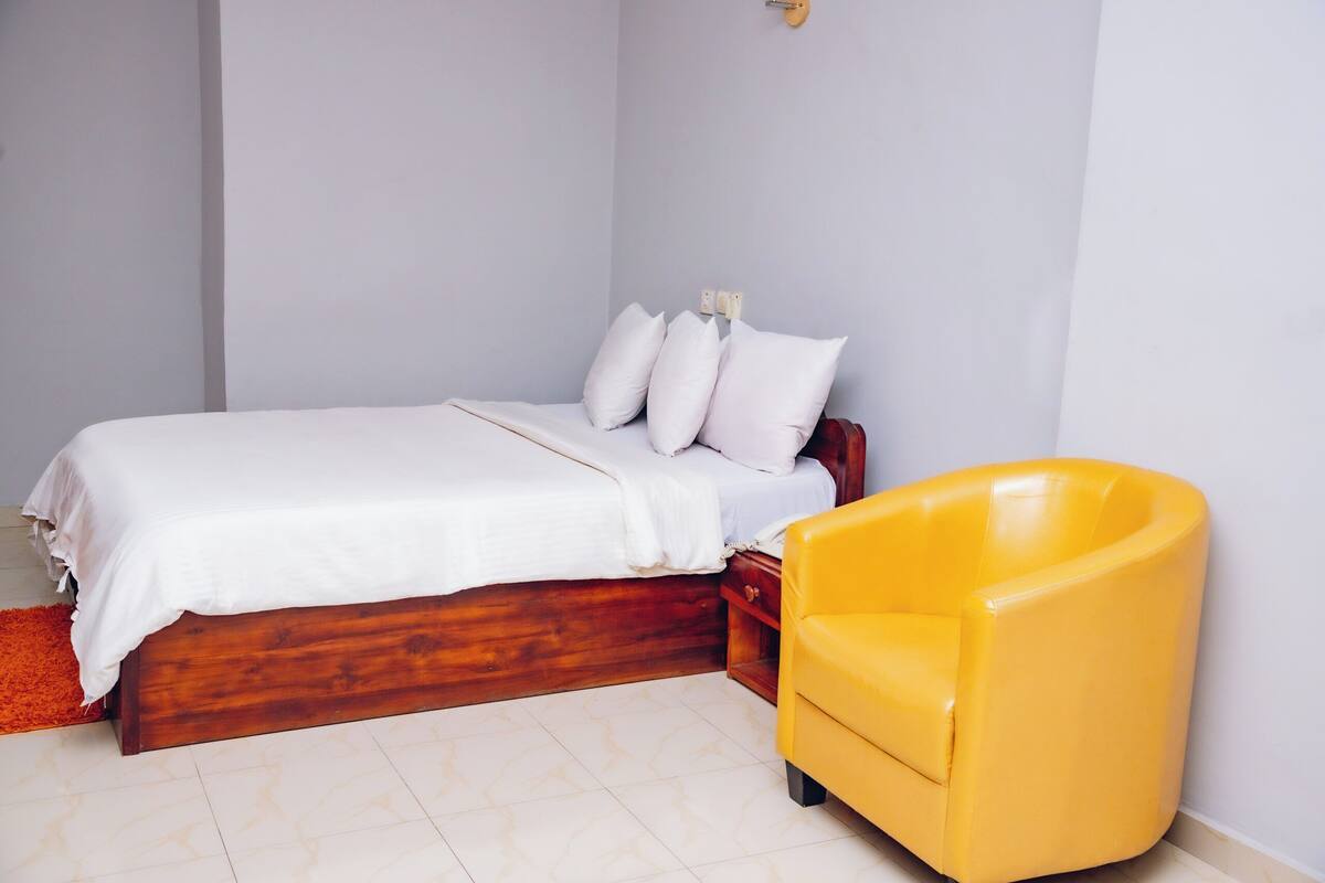 A bedroom with a wooden bed, white bedding, and a yellow armchair.