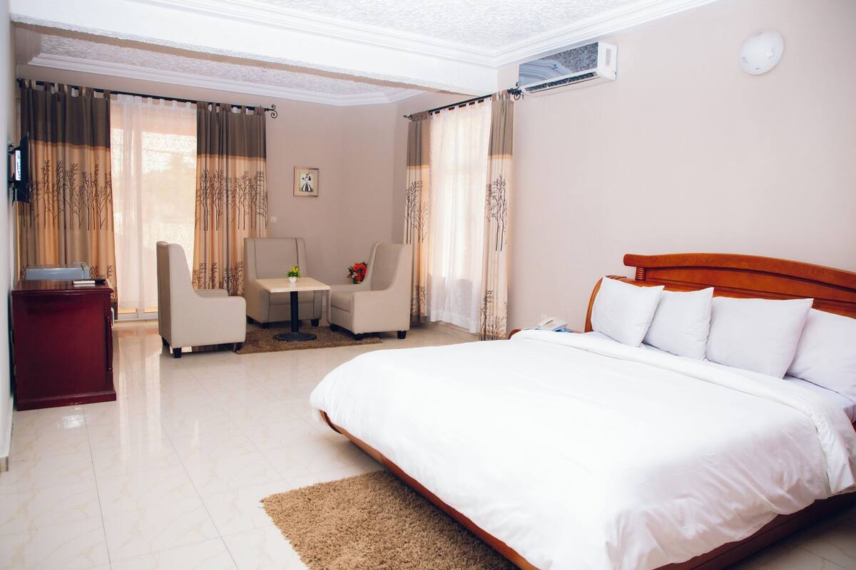 A hotel room with a large bed, a desk, a chair, and a small table with a vase of flowers.
