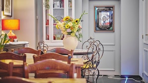 Un comedor con sillas de madera y una mesa, un florero con flores, una lámpara, un aparador con puertas de vidrio y un cartel enmarcado en la pared.