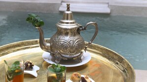 A tray with a teapot and glasses of tea, a small plate with a pastry, and a candle on a table near a pool. - Riad Vanilla Sma (Marrakech)