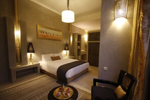 A hotel room with a large bed, bedside lamps, a painting on the wall, a small table with a tray of snacks, and a chair. - Riad Vanilla Sma (Marrakech)