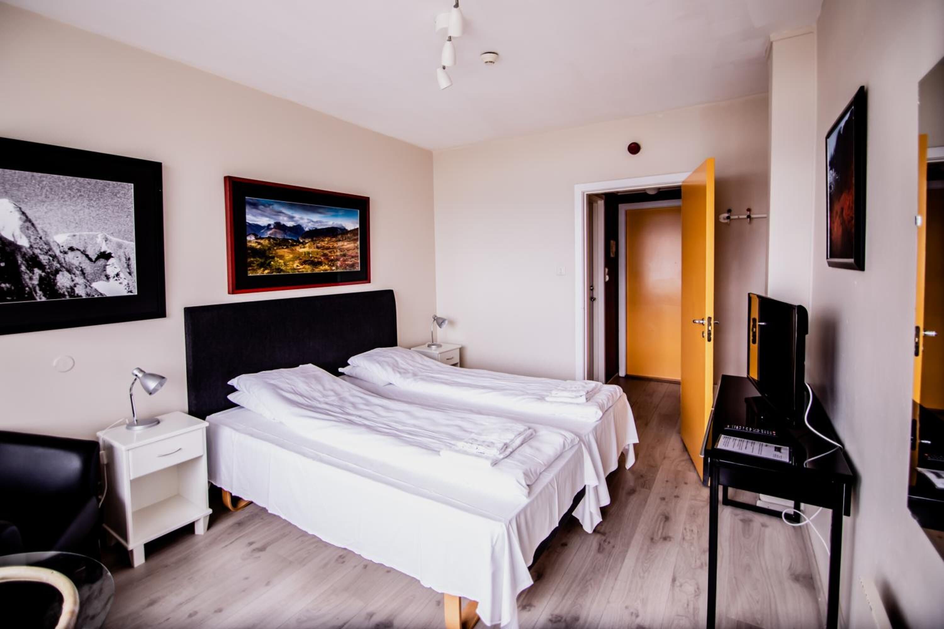 Una camera d'albergo con due letti, una scrivania con una lampada, un pianoforte e quadri appesi al muro.