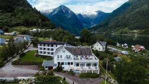 A large, white, multi-story building with a prominent entrance and a balcony, surrounded by lush greenery and a lake, with mountains in the background. - Kringsjå Hotell (Sogndal)