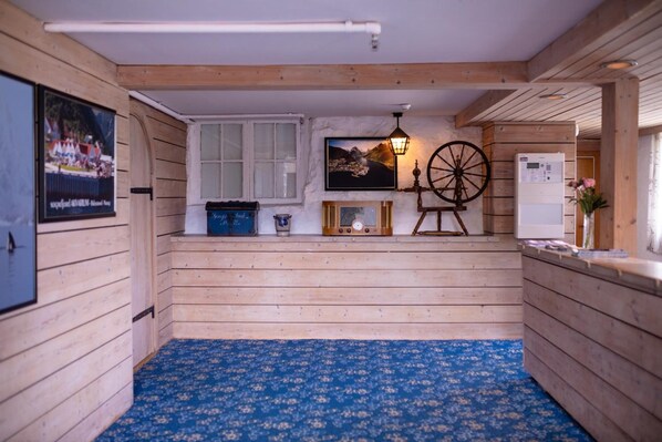 A wooden interior with a blue patterned carpet, a mounted television, a vintage-style lamp, and a refrigerator. - Kringsjå Hotell (Sogndal)