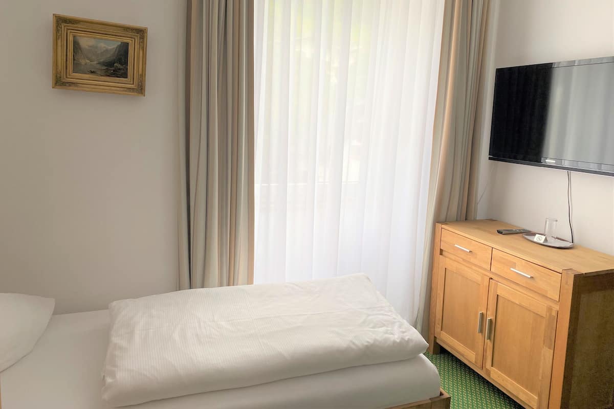Una habitación de hotel con una cama, un armario de madera, un televisor y un cuadro en la pared.