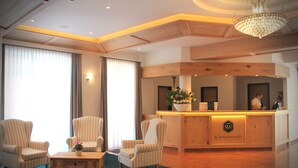 Un espace d’accueil avec un comptoir de réception en bois, un lustre et des fauteuils à rayures.
