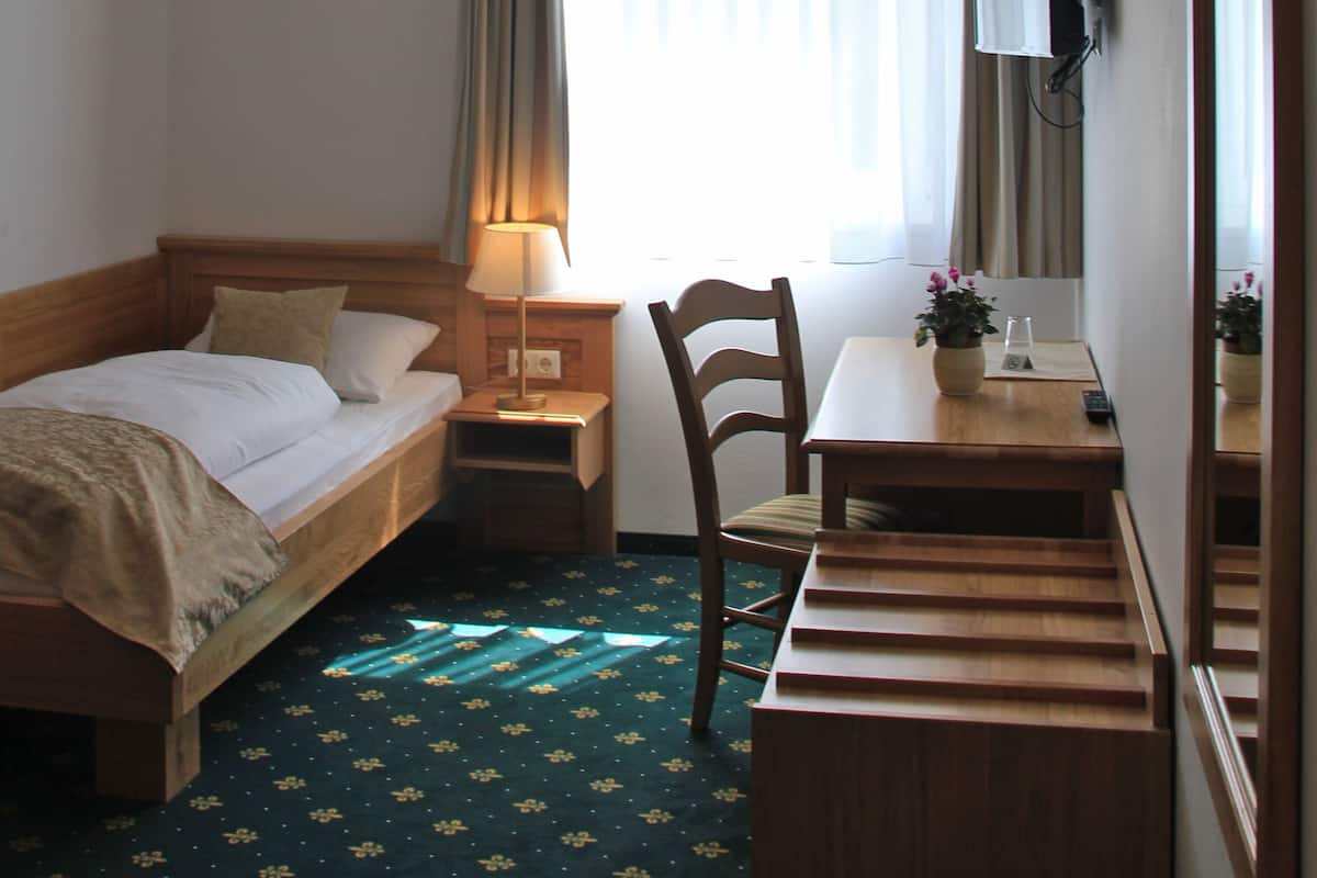Habitación de hotel con cama, escritorio, silla, televisor y ventana con cortinas.