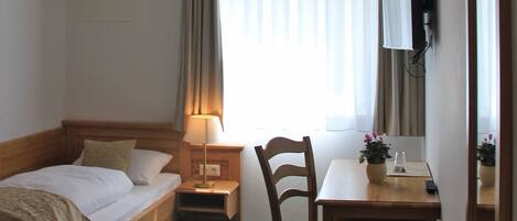 Une chambre d’hôtel avec un lit, un bureau et une chaise, une télévision et une fenêtre avec des rideaux.