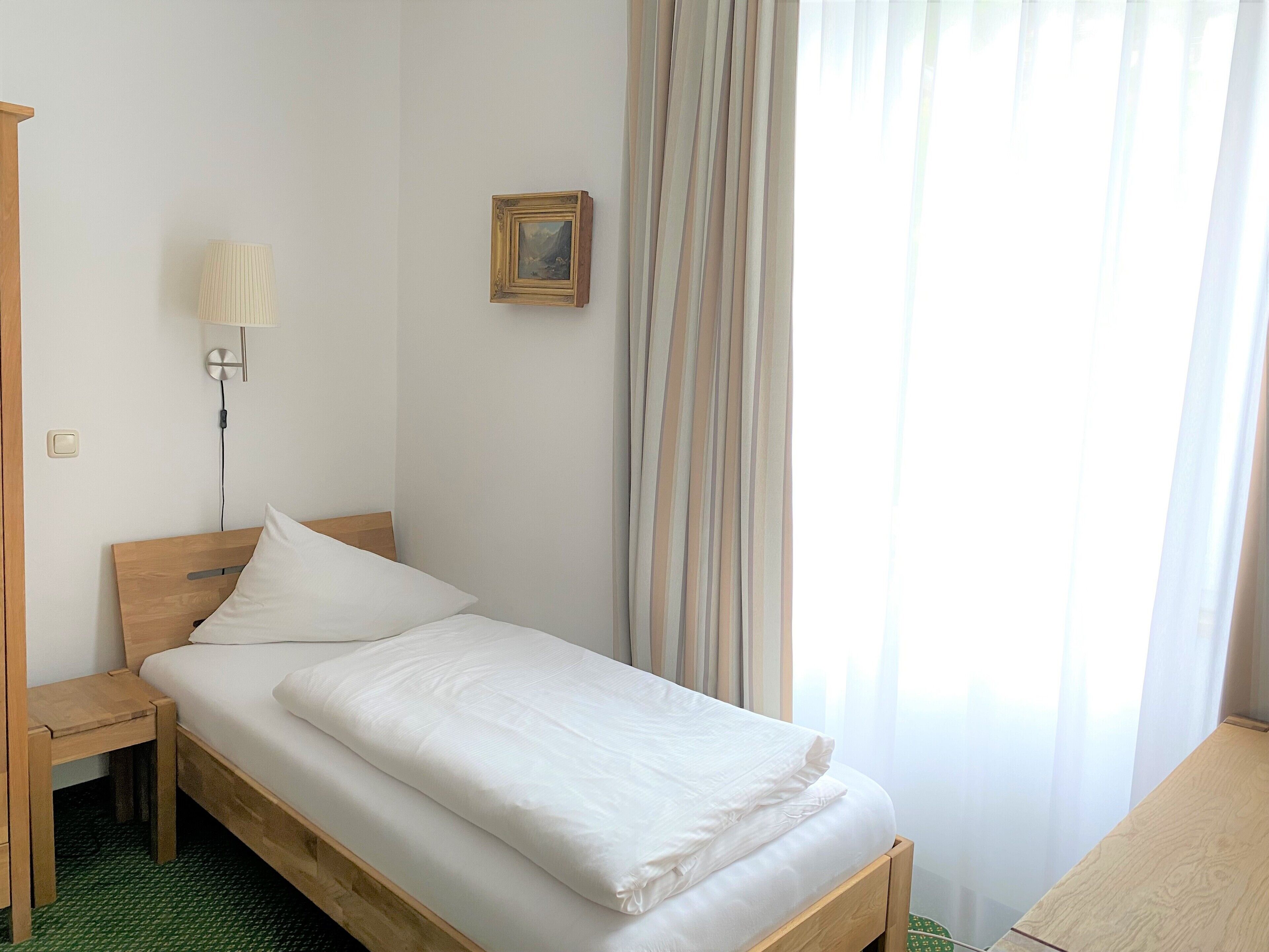 A neatly made bed with white linens in a room with a wooden headboard.